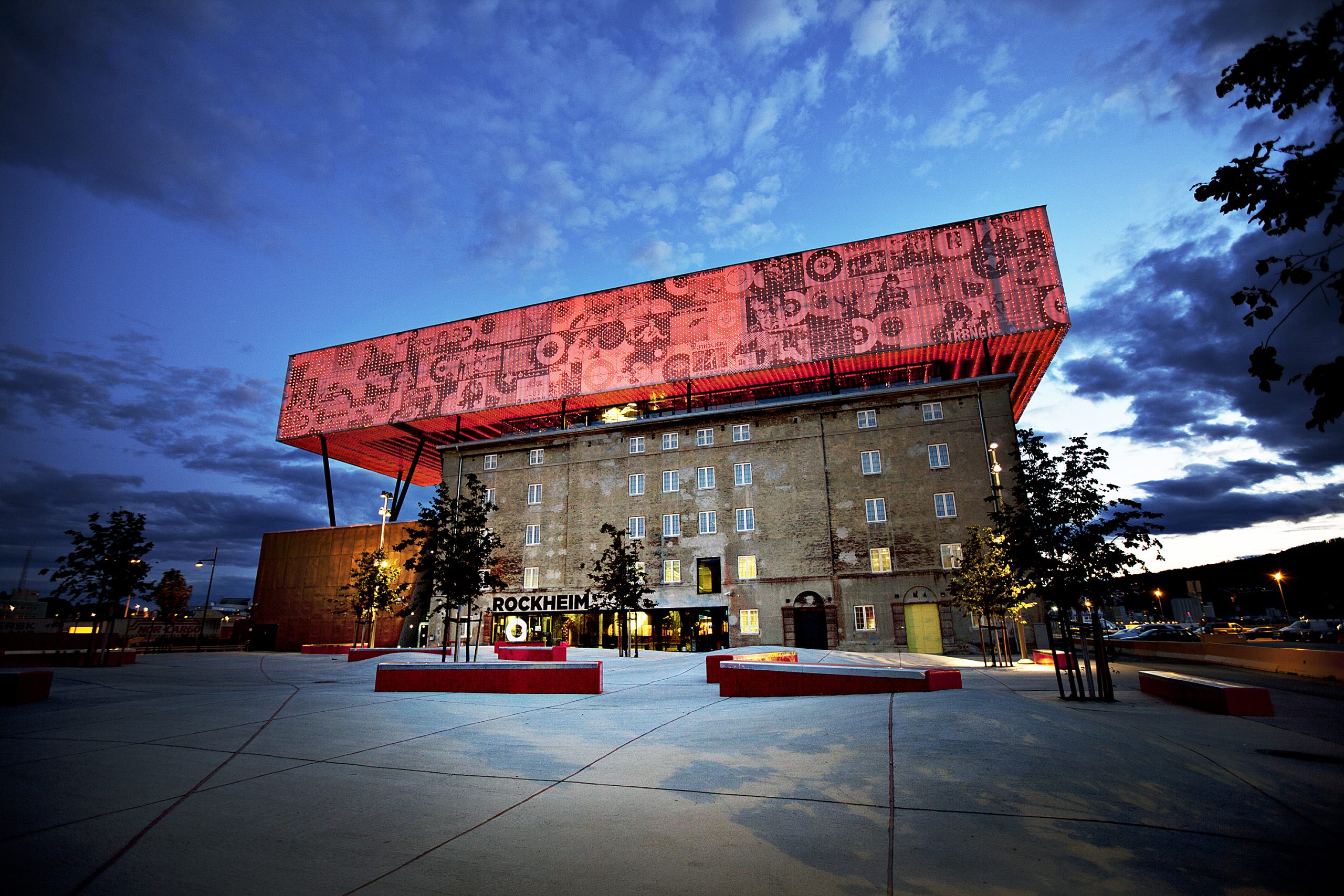 Foto Harald Øren.Rockheim A building in blue twilight, with red light screens on the roof.
